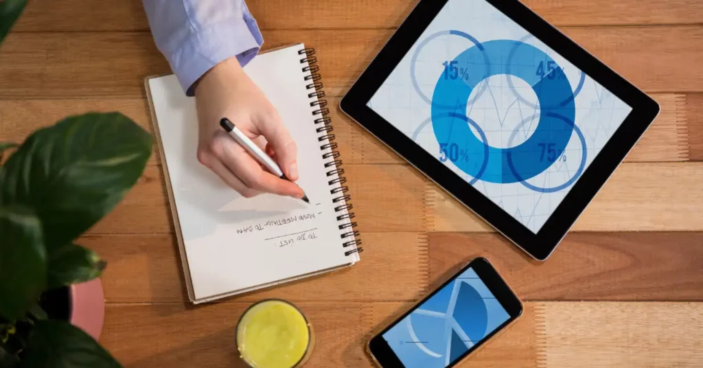 Imagem de uma pessoa anotando em um caderno, acompanhada de tablet e smartphone exibindo gráficos e dados em tempo real, destacando a importância de usar dados instantâneos para melhorar campanhas de marketing.