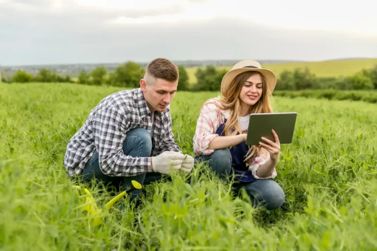 Homem e mulher no campo do agronegócio familiar usando tecnologia para atrair investimentos, com visual de céu nublado ao fundo.