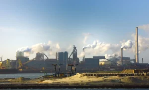 Vista panorâmica de uma grande indústria brasileira com fábricas, chaminés e fumaça no horizonte, perto de um cais e do mar, simbolizando crescimento industrial em 2025.