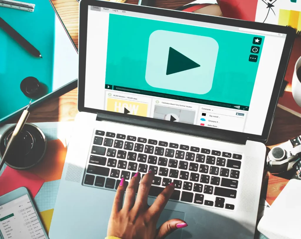 A Importância das Legendas e transcrições para conteúdos em Vídeo: pessoa digitando em um notebook com player de vídeo na tela, em um ambiente de trabalho com materiais de escritório ao redor