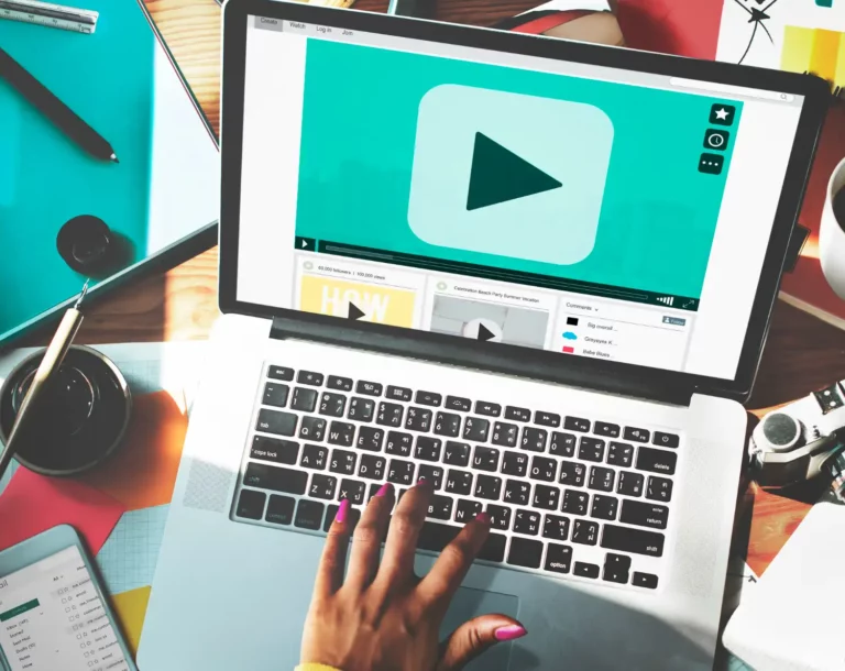 A Importância das Legendas e transcrições para conteúdos em Vídeo: pessoa digitando em um notebook com player de vídeo na tela, em um ambiente de trabalho com materiais de escritório ao redor