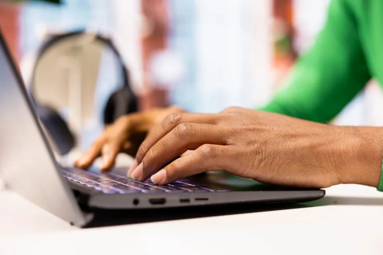Mãos usando um notebook em um ambiente de trabalho, com foco no teclado e na tela, transmitindo apoio e interação digital para acessibilidade no site. Como Tornar um Site Acessível para Pessoas com Deficiência Visual.