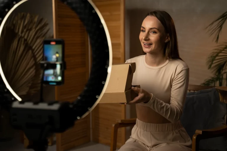 TikTok Shop no Brasil: O Que Aprender Com o Crescimento Acelerado da Plataforma: Pessoa em casa recebendo uma encomenda em uma caixa de papelão, em um ambiente iluminado, com celular sendo usado para gravar ou compartilhar o pedido em vídeo.